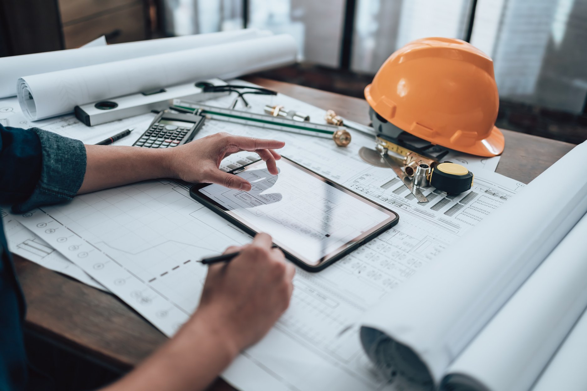 Engineering working with drawings inspection on tablet in the office and Calculator, triangle ruler, safety glasses, compass, vernier caliper on Blueprint. Engineer, Architect, Industry and factory concept.